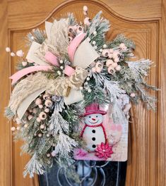 a snowman wreath hanging on the front door with pink and white flowers in it