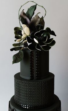 a three tiered black cake with flowers and leaves on the top, against a white background