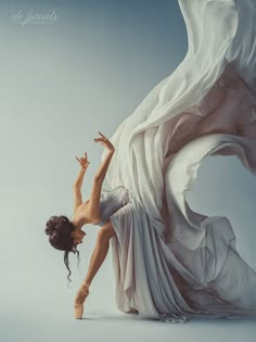 a woman in white dress standing on one leg with her arms up and legs spread out