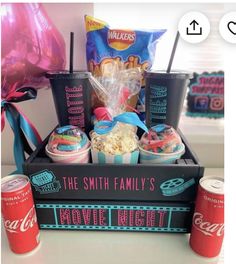 a box filled with cupcakes and snacks next to two soda cans on a table