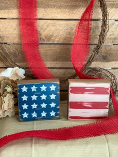 an american flag painted on wood blocks next to a red and white ribbon with flowers