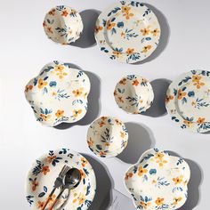 several plates and spoons are arranged on a white surface with orange flowers in them