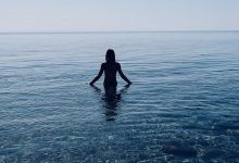 a person standing in the water with their back to the camera and arms spread out