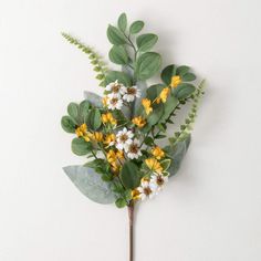 a bunch of yellow and white flowers with green leaves on a white wall behind it