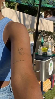 a woman with a small tattoo on her arm near an outdoor bbq and umbrella