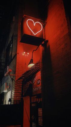 a red neon heart sign on the side of a brick building at night with street lights