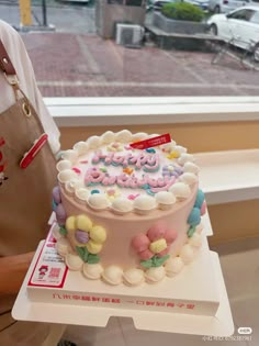 a person holding a cake with the words happy birthday on it in front of a window