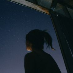 a person looking at the stars in the night sky from inside a building with a window