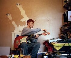 a man sitting on the floor playing an electric guitar in front of a wall that has been torn down