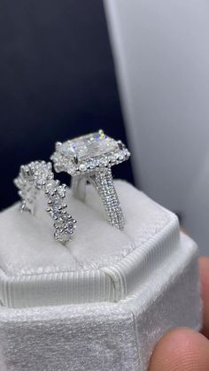 a pair of diamond rings sitting on top of a white cloth covered ring box in someone's hand