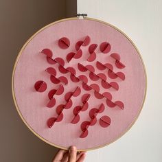 a person holding up a cross - stitch pattern in front of a white wall with pink background