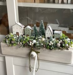 a white mantle with christmas decorations and greenery in front of a window sill