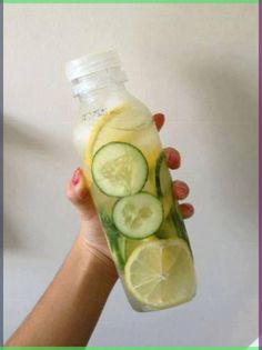 a person holding up a bottle with cucumbers and lemon slices in it,