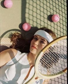 a woman laying on the ground with a tennis racket and balls in front of her