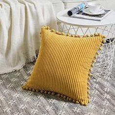 a yellow pillow sitting on top of a bed next to a white table and chair