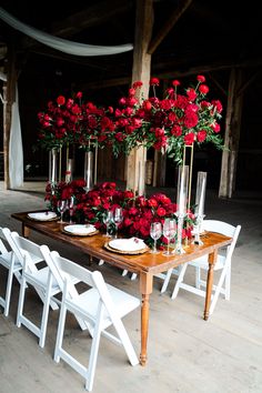 the table is set with white chairs and red roses in tall vases on each side