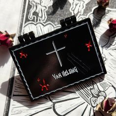 a small black box with a cross on it sitting next to some flowers and roses