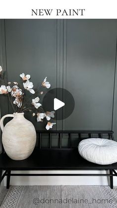 a white vase sitting on top of a black bench next to a flower pot and pillow