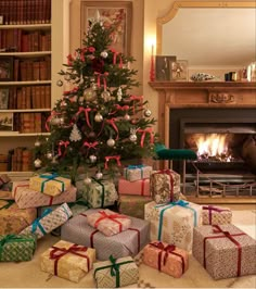 a christmas tree with presents under it in front of a fire place filled with books