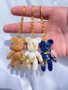 three small teddy bears are hanging from a gold - plated keychain in the palm of someone's hand