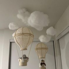 two hot air balloons floating in the sky with clouds above them and stuffed animals hanging from them