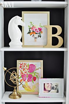 a white book shelf filled with pictures and vases on top of each other in front of a black wall