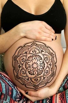 a pregnant woman sitting on top of a bed with her belly covered in intricate designs