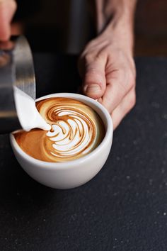 a person holding a spoon in a cup of coffee with liquid pouring out of it