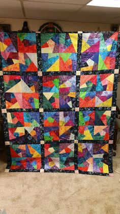 a quilt made with different colors and shapes on the floor in front of a wall