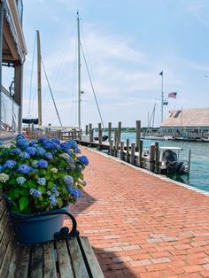 a wooden bench sitting on top of a brick walkway next to the water with boats in the background