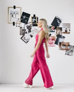 a woman is walking in front of a wall with pictures and frames on the wall