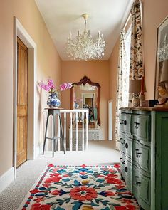 a room with a rug, dresser and chandelier hanging from the ceiling in front of a mirror