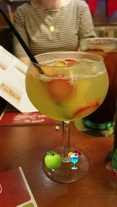 a woman sitting at a table in front of a glass filled with liquid and fruit