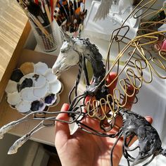 a person holding up some art pieces in their hands with other items on the table behind them