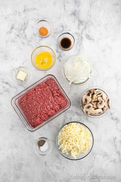 ingredients to make meatloaf laid out on a marble counter top, including eggs, mushrooms, cheese and sauces