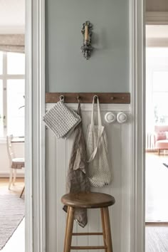 a wooden stool sitting in front of a white wall with two bags hanging on it