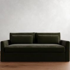 a green couch sitting on top of a wooden floor next to a white wall in an empty room