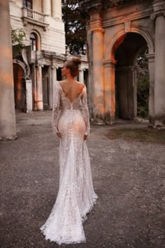 a woman in a white wedding dress is standing on the ground near an old building