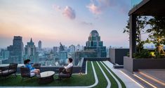 two people sitting on chairs in front of a cityscape at dusk with the sun setting