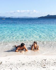 two people laying on the beach in shallow water