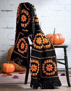 an orange and black crocheted blanket sitting on top of a chair next to pumpkins