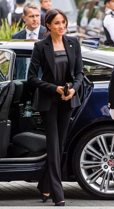 a woman in black suit and heels stepping out of a car with her hand on the door