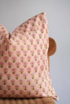 a pink flowered pillow sitting on top of a wooden chair