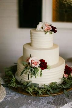 a three tiered white wedding cake with red and pink flowers