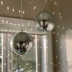 two disco balls hanging from the ceiling in front of a window with lights on it