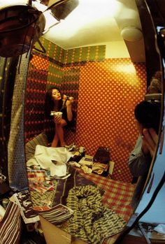 a woman taking a selfie in a mirror with clothes on the floor and other items scattered around