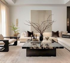 a living room filled with white couches and black coffee table in front of a painting