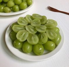 two white bowls filled with green grapes next to a fork