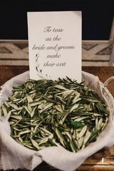 a bowl filled with green leaves next to a sign that says to toss as the bride and groom make their exit