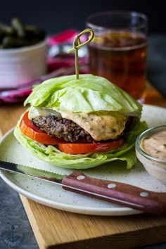 a hamburger with lettuce and tomatoes on a plate next to a knife, bowl of dipping sauce